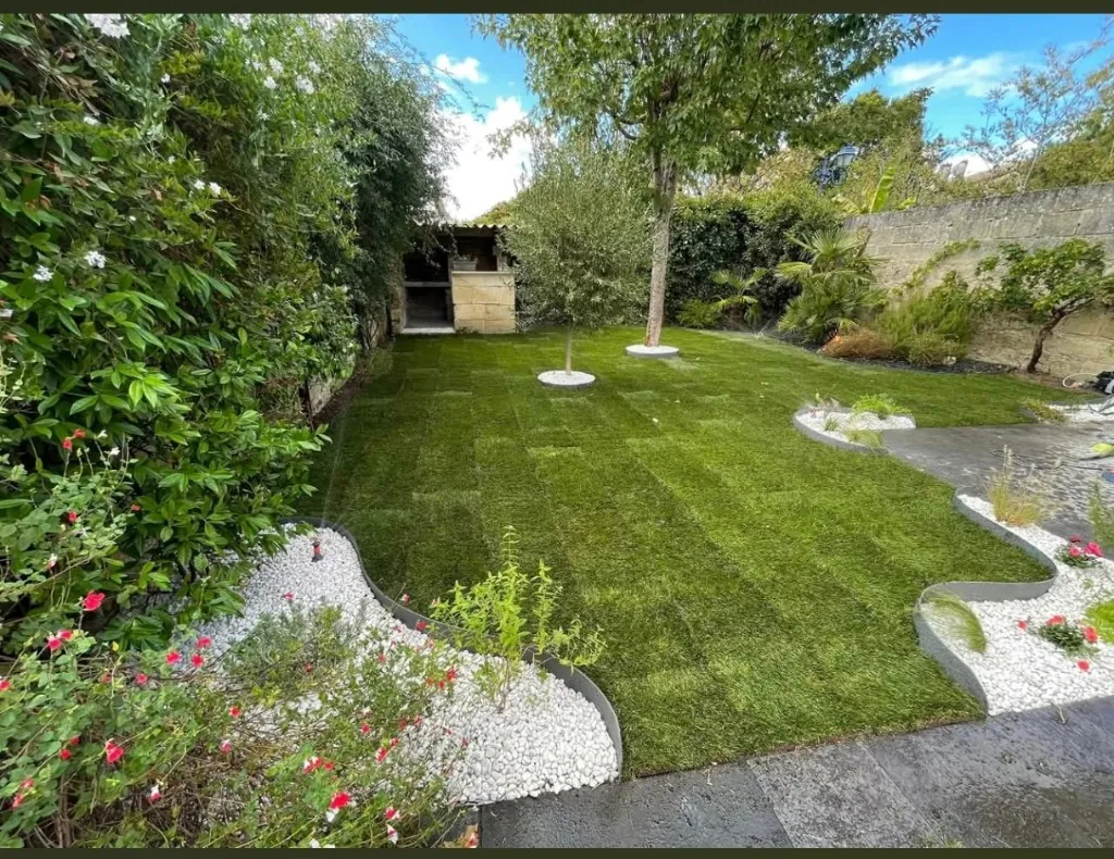 Jardin paysagé avec pelouse verte, massifs fleuris et bordures galets après travaux